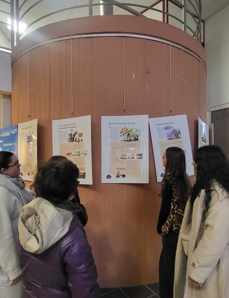 Image 1 : Des élèves lisent des affiches sur la laïcité apposées sur un pilier circulaire du Lycée